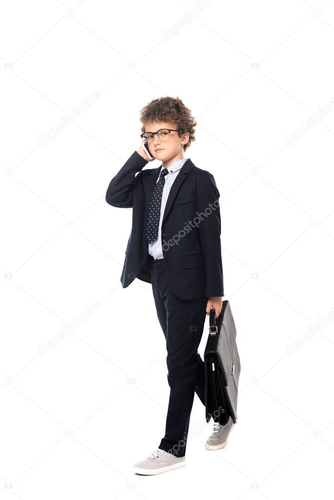 boy in suit and glasses holding briefcase while talking on smartphone isolated on white