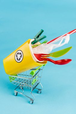 Sarı geri dönüşüm kutusu. Mavi arka planda küçük alışveriş arabasında plastik var.