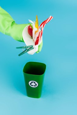 Lastik eldivenli temizleyicinin mavi arka plandaki çöp kutusuna plastik çöp atması, panoramik çekim