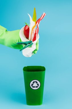 Lastik eldivenli temizleyicinin mavi arka plandaki çöp kutusuna plastik çöp atması, panoramik çekim