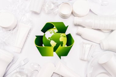 Geri dönüşüm işaretinin üst görünümü ve beyaz arkaplana saçılmış plastik çöpler