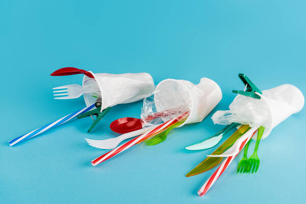 plastic cups with disposable cutlery on blue background