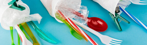 крупный план пластиковых чашек с одноразовыми столовыми приборами на синем фоне, панорамный снимок