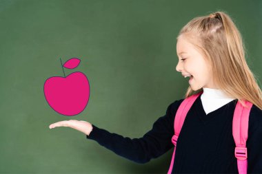 Okullu kız, yeşil karatahtadaki resimli pembe elmayı gösteriyor. 