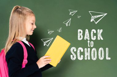 Yeşil karatahtanın yanında kitap okuyan okul kızlarının yan görünüşü