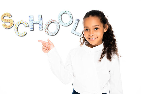 african american schoolgirl pointing with finger at school lettering while looking at camera isolated on white