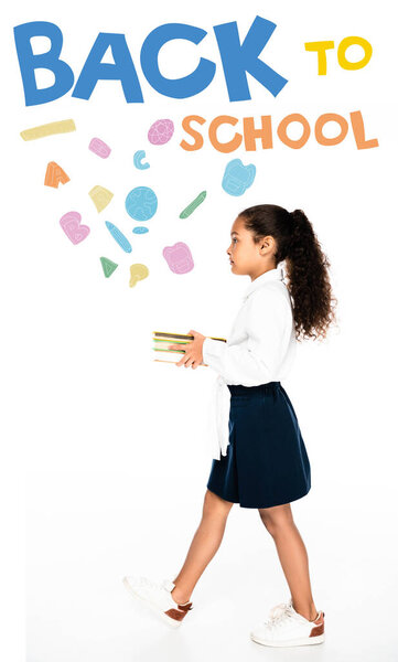 side view of african american schoolgirl walking while holding books on white background, back to school illustration