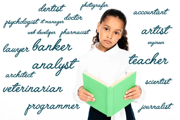 upset african american schoolgirl looking at camera while holding book isolated on white with various professions illustration