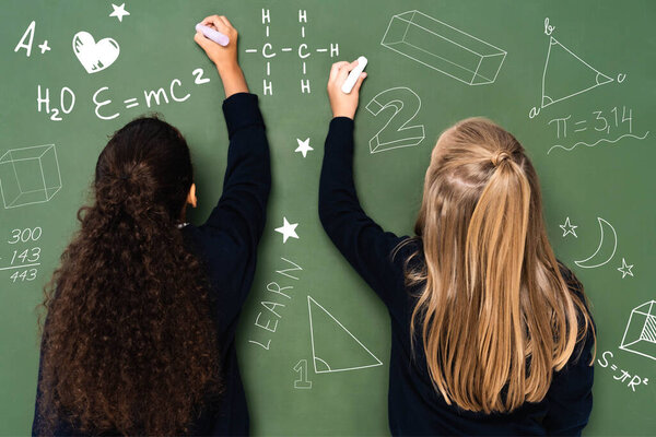 back view of multicultural schoolgirls writing on chalkboard