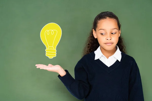 Skeptical Schoolgirl Pointing Hand Light Bulb Green Chalkboard — Stock Photo, Image