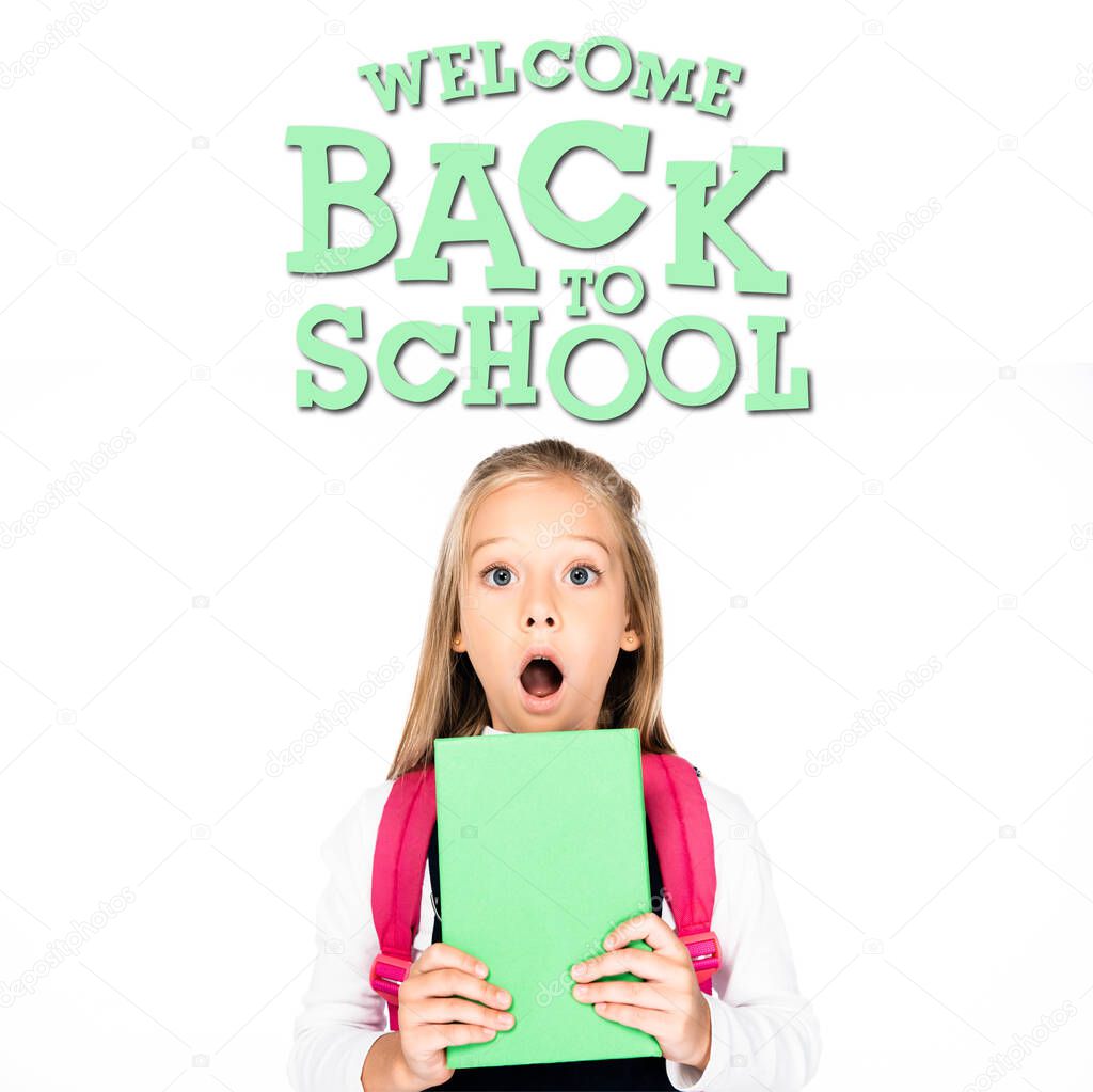 shocked schoolgirl holding book while looking at camera isolated on white, welcome back to school illustration