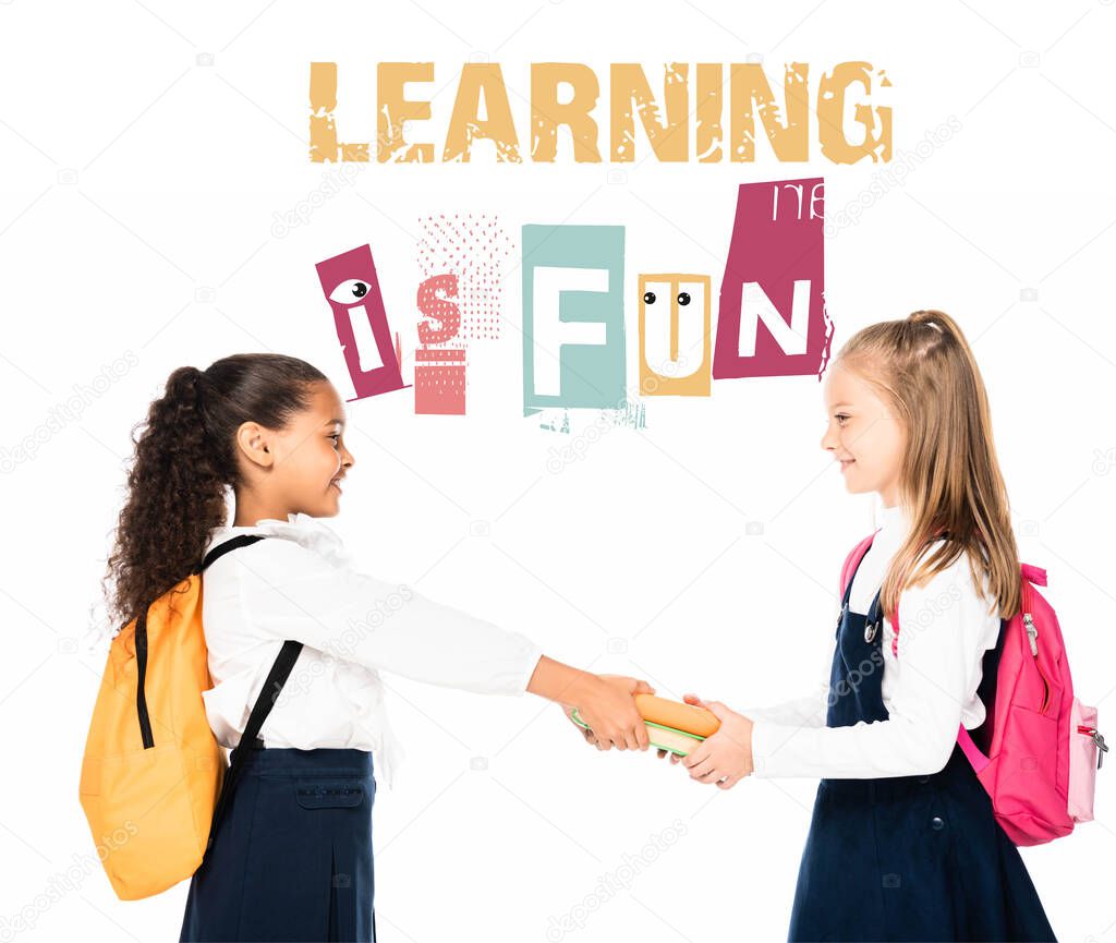 side view of african american schoolgirl giving books to smiling friend isolated on white, learning is fun illustration