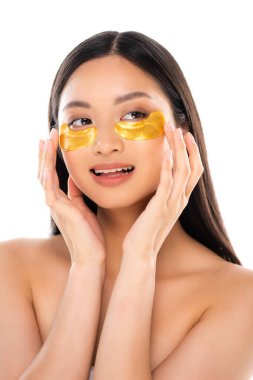 Asyalı çıplak bir kadın, beyaz üzerinde izole edilmiş altın göz bantlarına dokunurken gözlerini kaçırıyor.