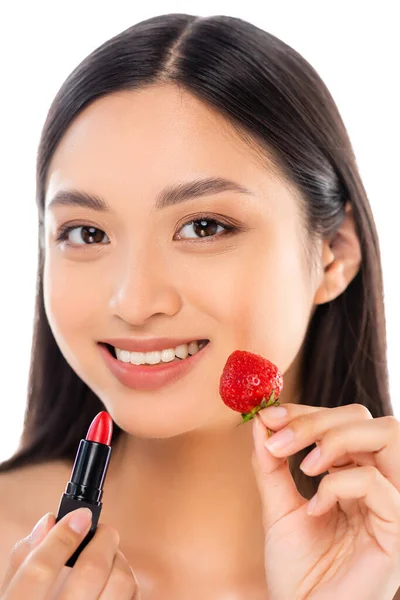 年轻的亚洲女人一边拿着红色口红和新鲜草莓 一边看着相机 脸被白色隔开 — 图库照片