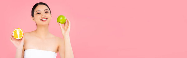 panoramic concept of asian woman holding whole apple and half of juicy orange isolated on pink 
