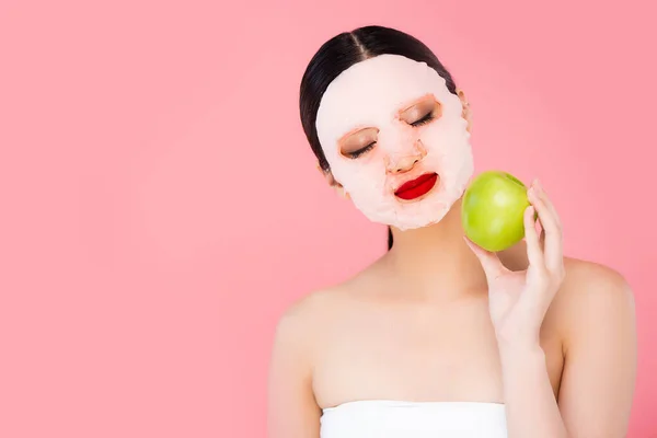 ピンクに隔離された緑のリンゴを持つ顔のマスクの若いアジア人女性 — ストック写真