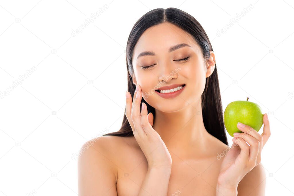 Excited young asian woman with closed eyes touching face and holding apple isolated on white