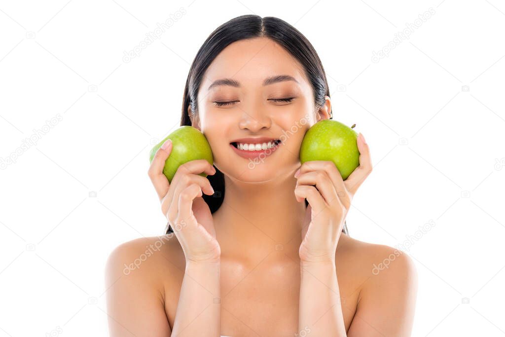 Excited young asian woman with closed eyes holding apples isolated on white