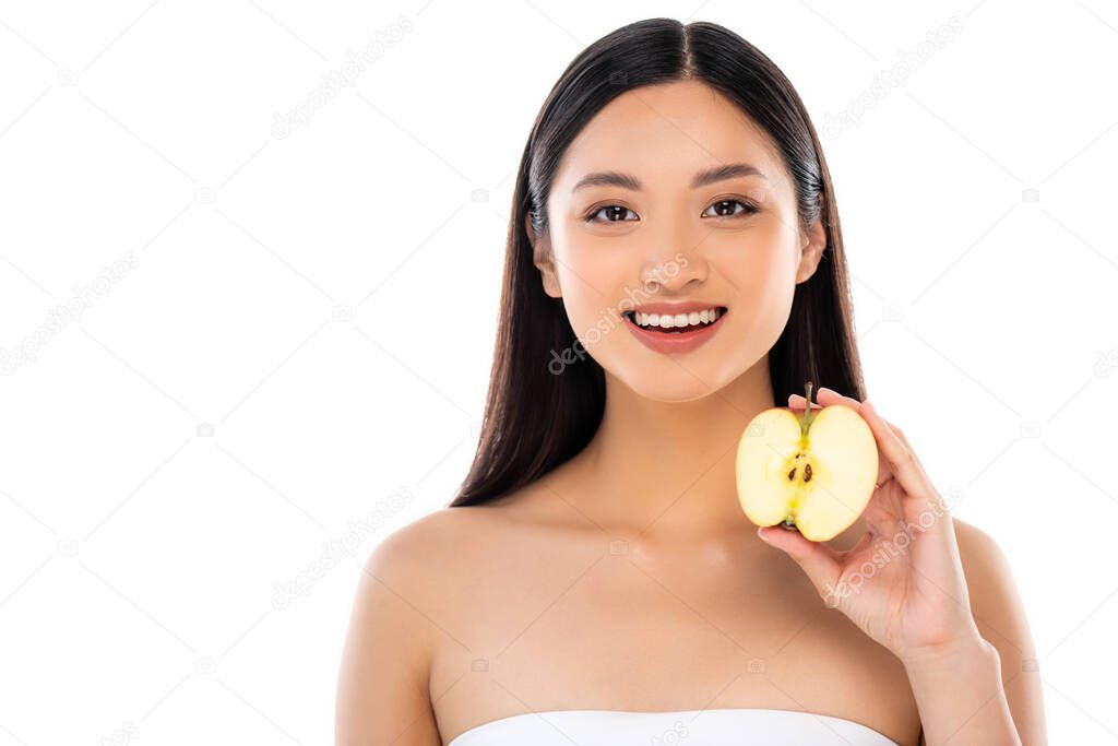 brunette asian woman looking at camera while holding half of ripe apple isolated on white