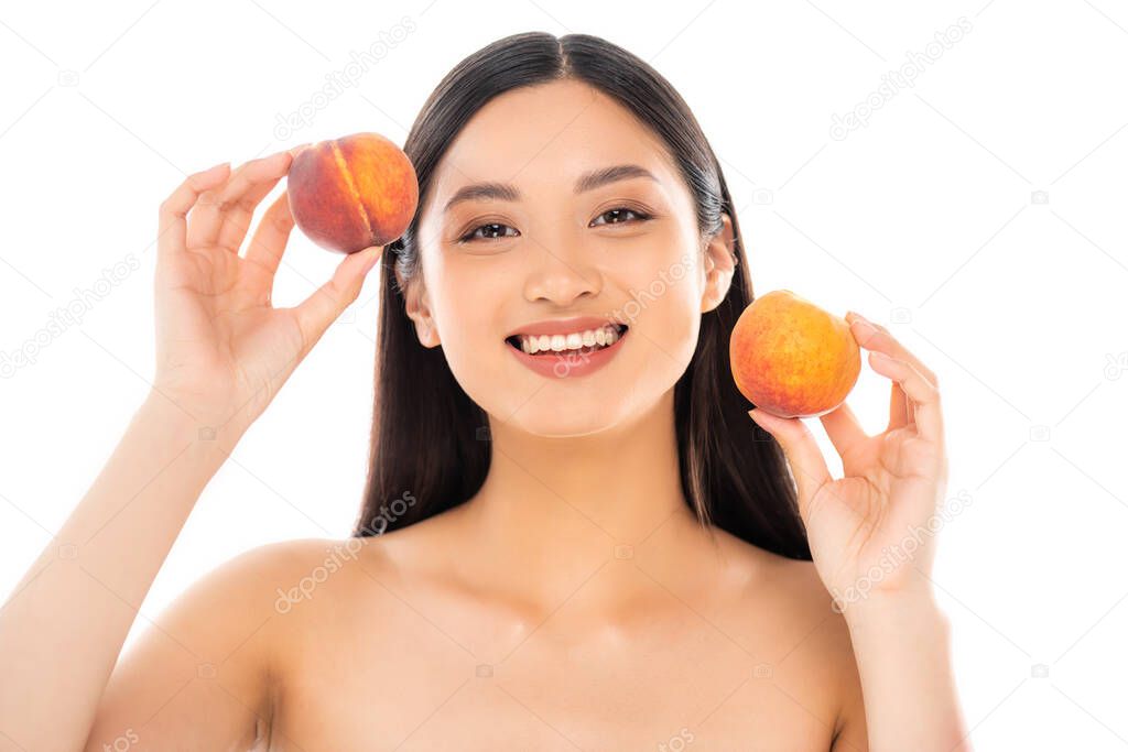 naked asian woman holding ripe peaches while looking at camera isolated on white