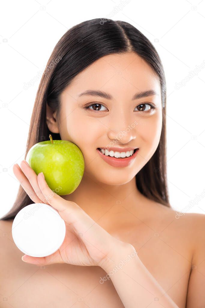naked asian woman holding ripe green apple and cosmetic cream near face isolated on white
