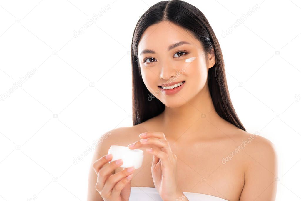 brunette asian woman touching cosmetic cream while looking at camera isolated on white