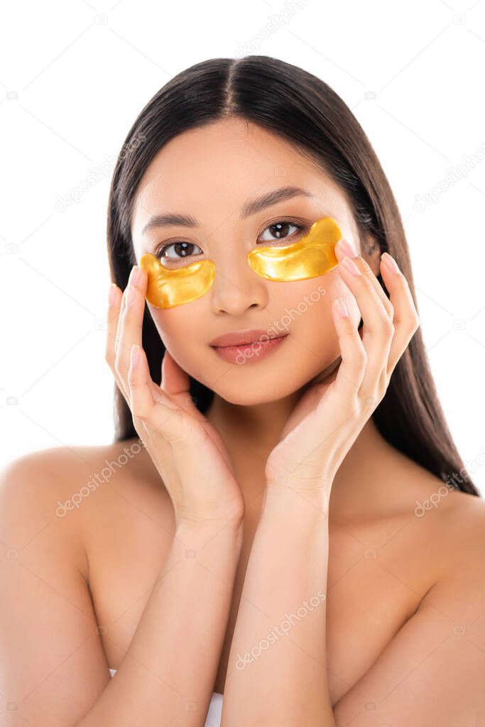 brunette asian woman looking at camera while touching golden eye patches isolated on white