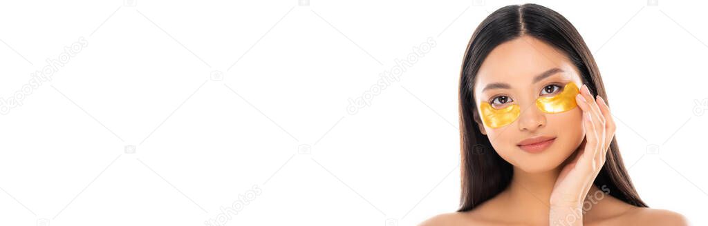 horizontal image of asian woman touching golden eye patch on face while looking at camera isolated on white
