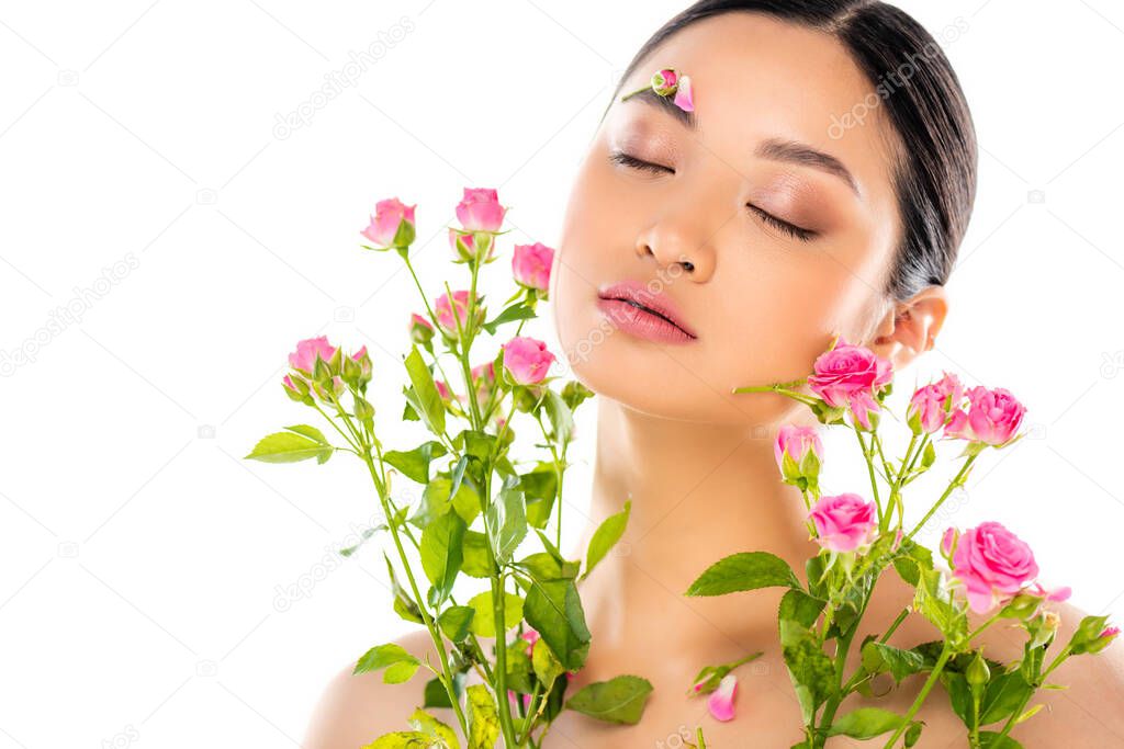 sensual asian woman with floral decoration on face near pink roses isolated on white
