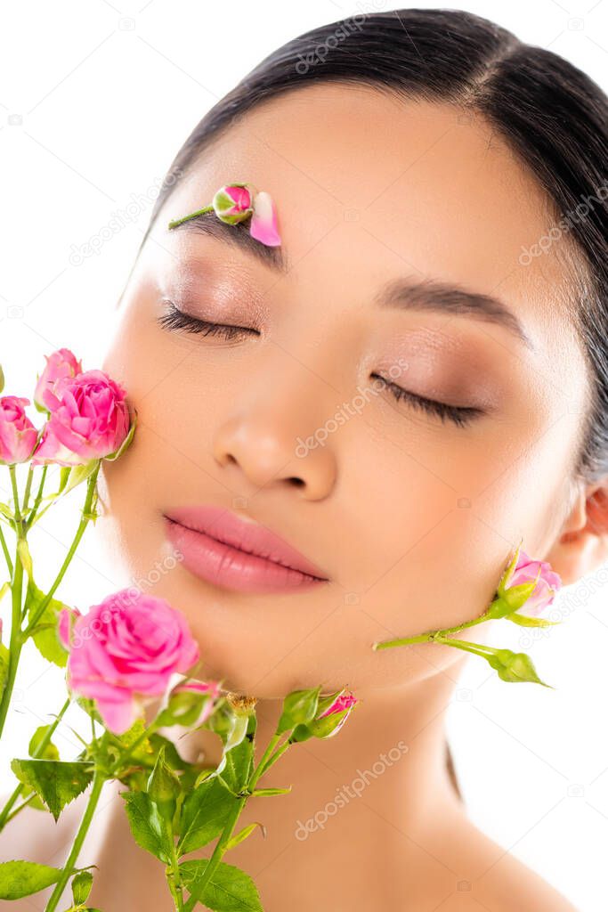 portrait of sensual asian woman with closed eyes, flowers on face, near tiny roses isolated on white