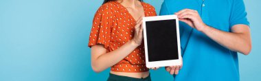 Bluz giyen kadın ve polo tişörtlü adam kısmen mavi, yatay görüntüde boş ekranlı dijital tablet gösteriyor
