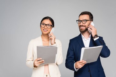 Gri renkte izole edilmiş cep telefonlarıyla konuşan ve klasörler tutan ırklar arası iş ortakları.