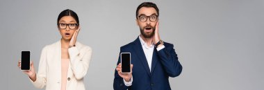 Beyaz ekranlı akıllı telefonlar gri, yatay konseptte izole edilirken yüzlere dokunan ırklar arası iş insanları şok oldu.