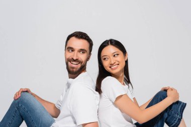 Esmer, Asyalı bir kadın ve beyaz tişörtlü, sakallı bir adam sırt sırta oturuyorlar.