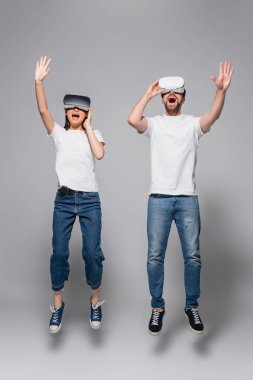 excited couple in vr headsets, jeans and white t-shirts waving hands while levitating in vr headsets on grey clipart