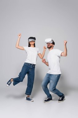 VR kulaklıklı, kot pantolonlu, beyaz tişörtlü gri renkte dans eden genç, heyecanlı bir çift.