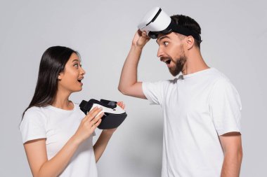 young asian woman in white t-shirt holding vr headset while looking at excited man on white