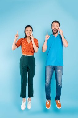 Akıllı telefonlardan konuşan ve mavi renkte uçarken fikir işareti gösteren heyecanlı ırklar arası bir çift.