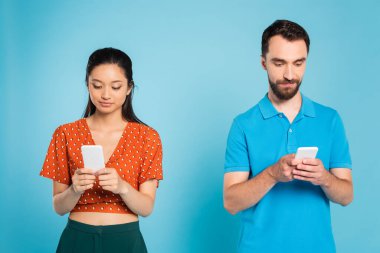Kırmızı bluzlu genç Asyalı kadın ve polo tişörtlü sakallı adam mavi üzerine akıllı telefon kullanıyor.