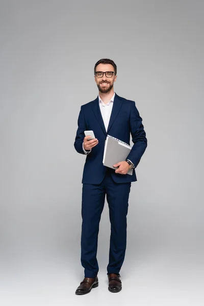 Vousatý Podnikatel Modrém Obleku Brýle Drží Smartphone Složku Šedé — Stock fotografie