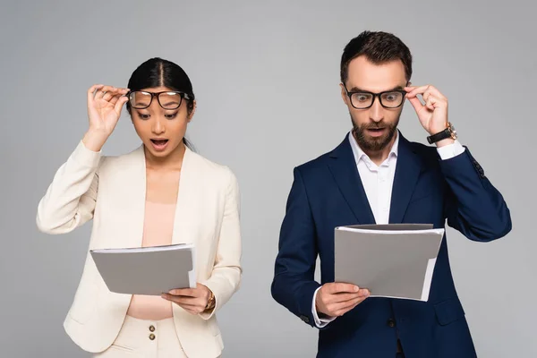 Sorprendidos Socios Comerciales Interracial Mirando Documentos Tocando Gafas Aisladas Gris — Foto de Stock