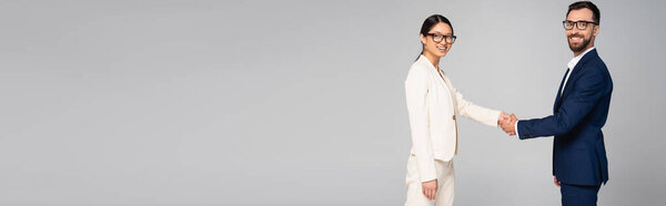 горизонтальный урожай межрасовых деловых партнеров, пожимающих руки, глядя на камеру, изолированную на сером