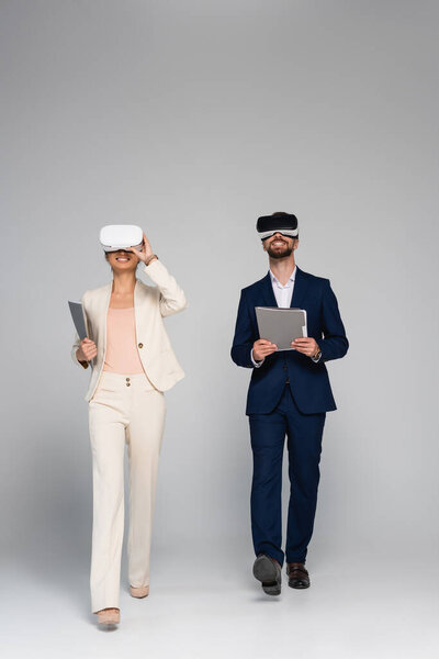 full length view of business partners in vr headsets holding folders while walking on grey