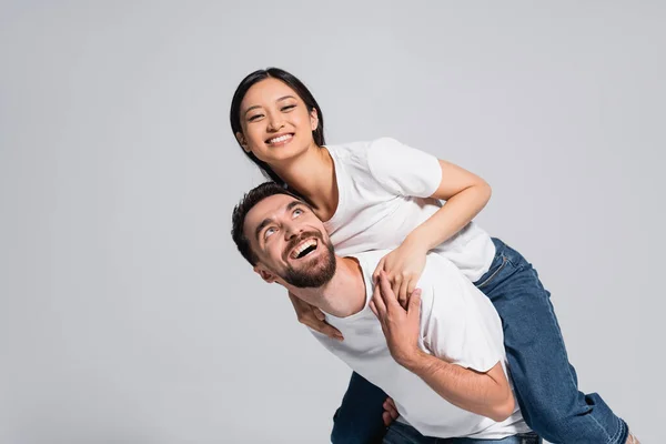 Excitado Hombre Blanco Camiseta Piggybacking Asiático Novia Aislado Gris — Foto de Stock