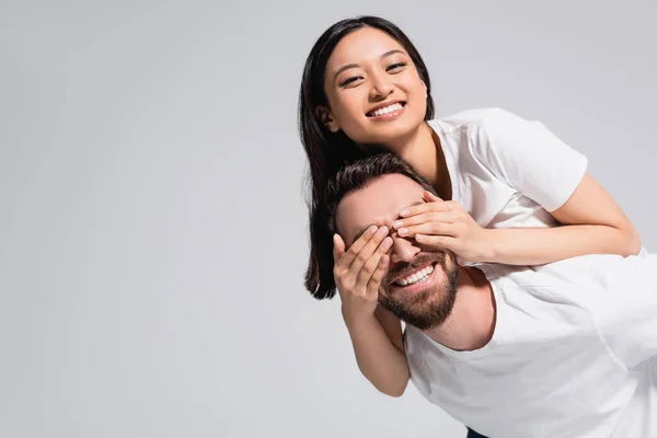 Excited Man Piggybacking Asian Girlfriend Covering His Eyes Hands Isolated — Stock Photo, Image