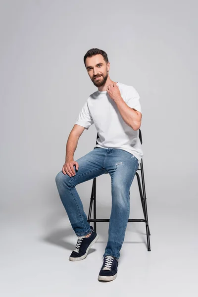 Jovem Homem Barbudo Shirt Branca Jeans Sentado Cadeira Enquanto Olha — Fotografia de Stock