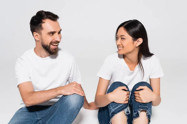 Pasangan Muda Interrasial Dengan Kaos Putih Saling Memandang Sambil Duduk — Stok Foto
