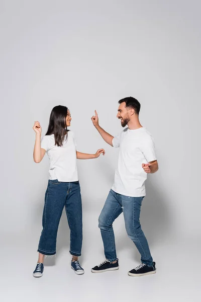 young interracial couple in jeans, white t-shirts and gumshoes dancing while looking at each other on white