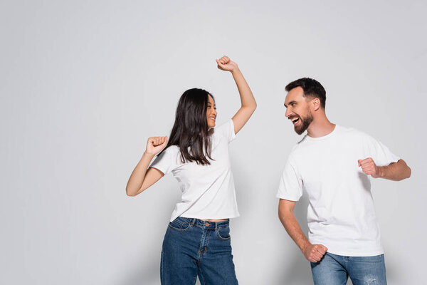young interracial couple in white t-shirts dancing while looking at each other on white