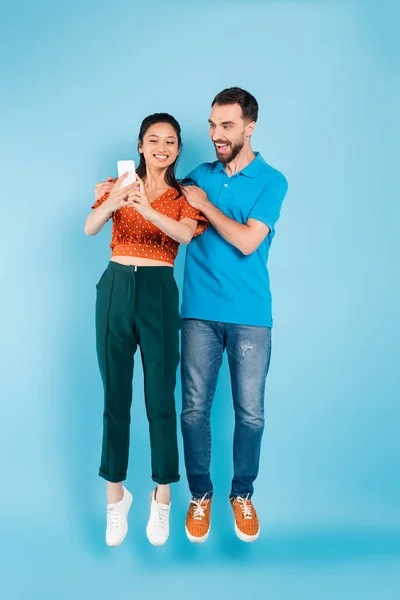 Excited Man Touching Shoulders Asian Girlfriend Using Smartphone While Levitating — Stock Photo, Image